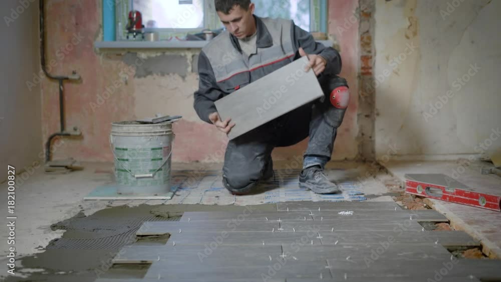 Repairman is laying tiles on the floor. Repairman is laying tiles on the floor.