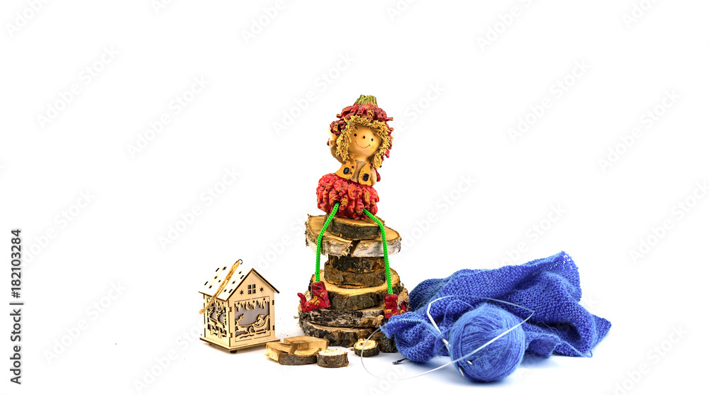 Doll on wooden round logs, knitting yarns and a house