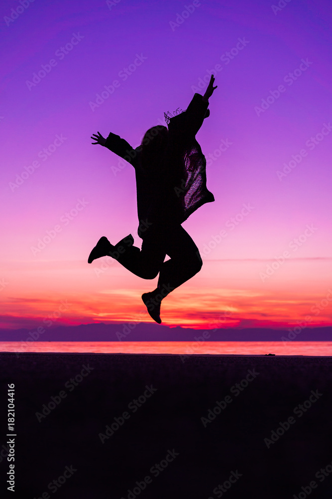 Sihouette of Happy Woman Jumping with Joy , against beautiful after sunset purple color tones by the sea