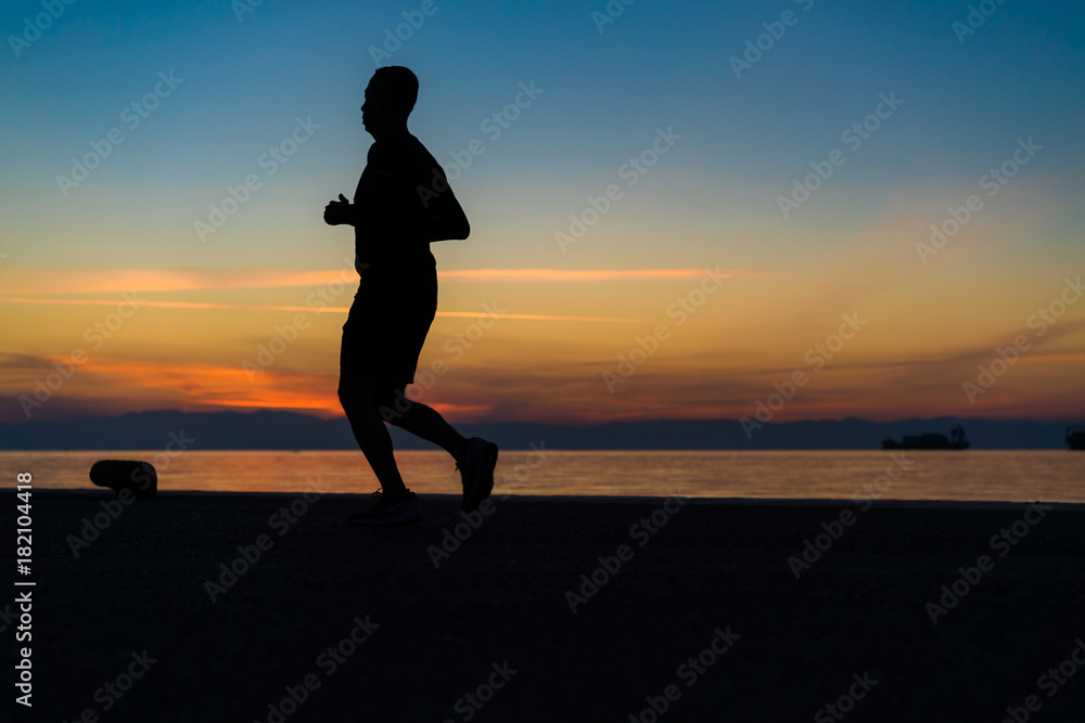 Sihouette of Young Man Running by the Sea, against beautiful after sunset color tones