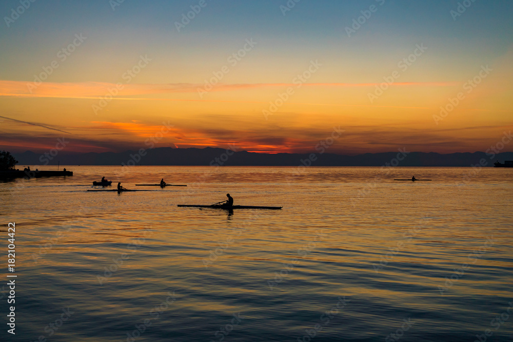 Tranquil scene of sea with rowing boats, against beautiful after sunset color tones Tranquil scene of sea with rowing boats, against beautiful after sunset color tones