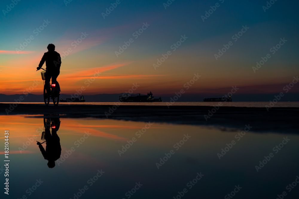 Silhuette of Man on Bicycle and his reflection on water from rain, against Lovely Colors Sky
