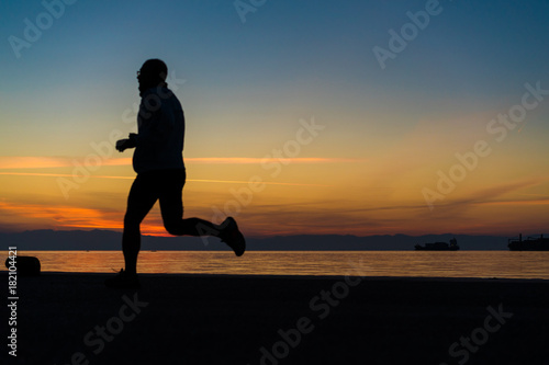 Sihouette of Man Wearing Glasses  Running by the Sea  against beautiful after sunset color tones
