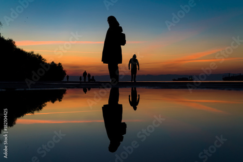 The Traveler... Reflection on Water after Rain of Womans Silhouette Standing by the Sea, against beautiful after sunset color tones