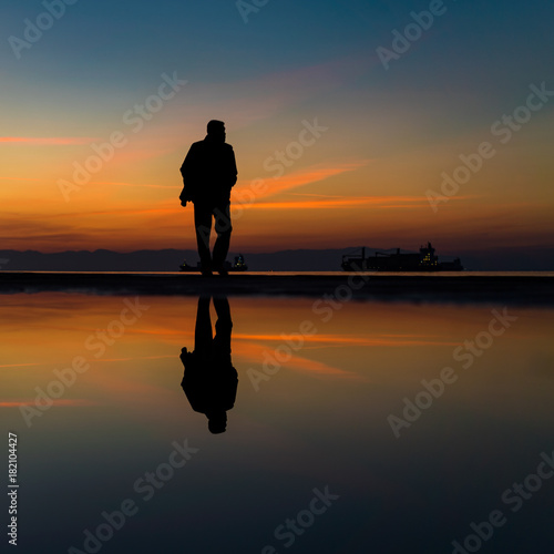 Keep on Walking... Reflection on Water after Rain of Mans Silhouette Walking by the Sea, against beautiful after sunset color tones