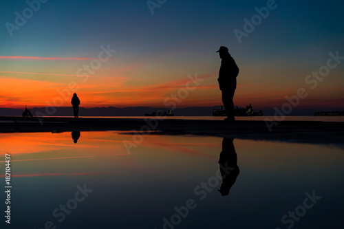 Reflections of People Silhouettes Standing by the Sea, against beautiful after sunset color tones