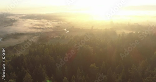 Aerial drone shot of fog covered countryside, forests and river flying into the Sun during sunrise photo