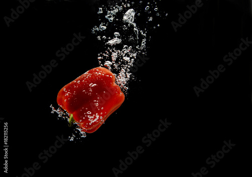 Red bell pepper falling under water with trail of bubbles