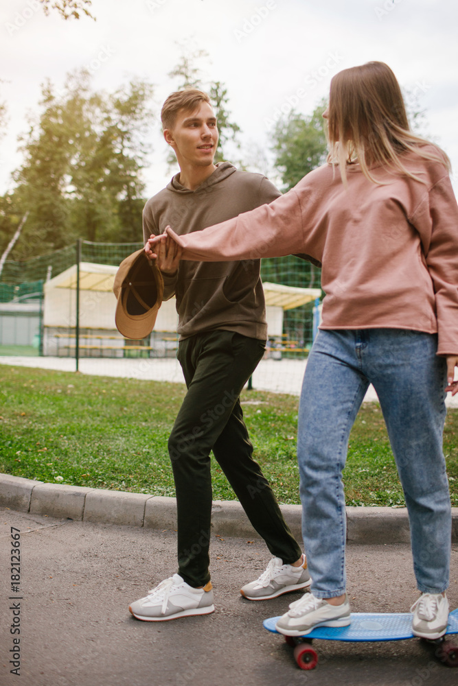 Teenage date in a park. Girl gets skateboarding lessons. Romance flirting and young love concept