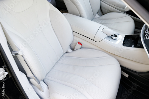 White perforated leather interior of the luxury modern car. Leather comfortable white seats and multimedia. Steering wheel and dashboard. automatic gear stick. © Aleksei