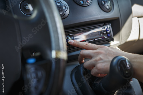 person in car presses radio button. Hand on background of dashboard of car.