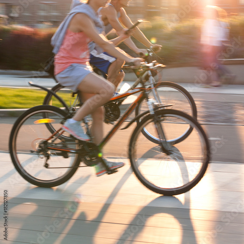 a boy and a girl ride bicycles down the street on a sunny summer day