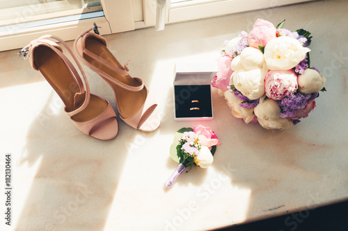 Wedding rings in white box, beige sandals, a bouquet of flowers and boutonniere at the window. Accessories for wedding. The symbols of love, wedding rings,shoes, wedding bouquet. Tonted photo. photo