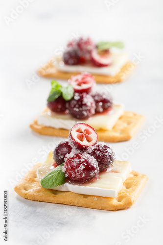 Crackers with brie, cranberries and mint on light background 