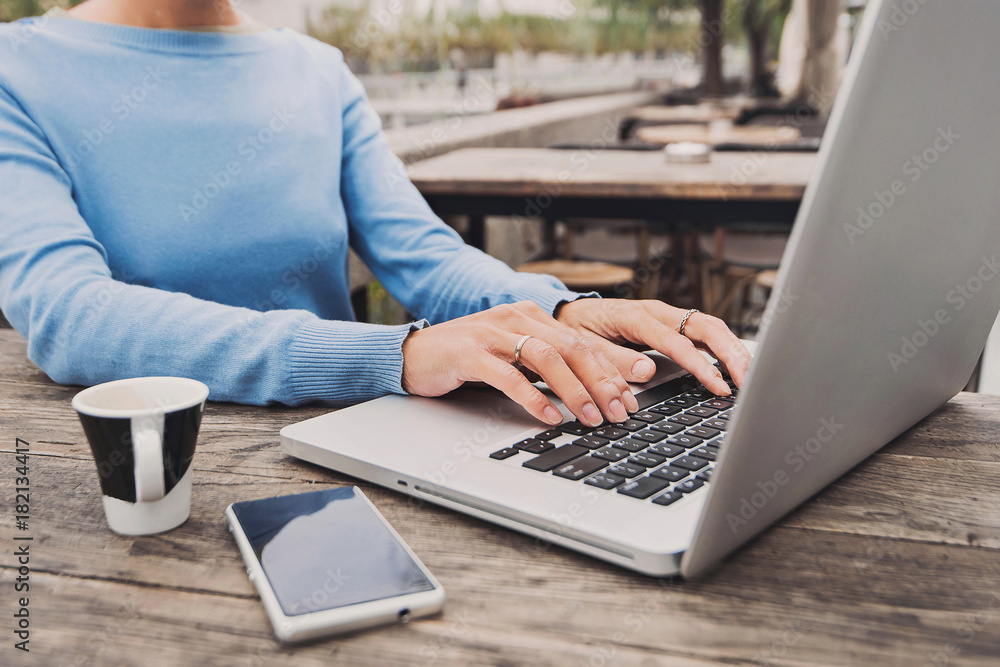 Fototapeta premium Young woman using laptop at cafe outdoors. Young girl sitting in a coffee shop and working on computer in a city