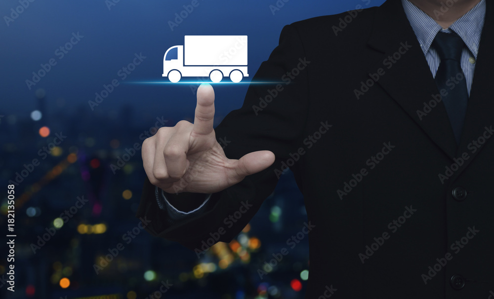 Businessman pressing truck flat icon over blur colorful night light city tower, Business transportation service concept Businessman pressing truck flat icon over blur colorful night light city tower, Business transportation service concept