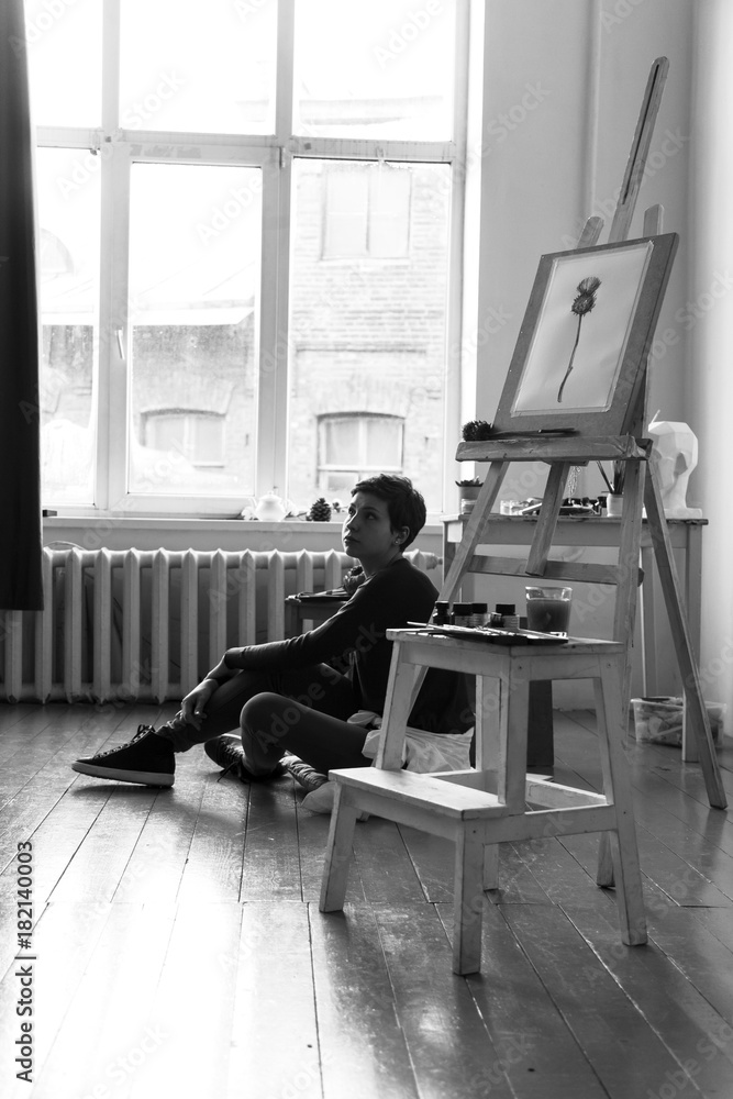 Female artist in her spacious white studio working with watercolor painting.  Natural lighting. Disclosure of creativity concept. Vertical composition. Black and white image