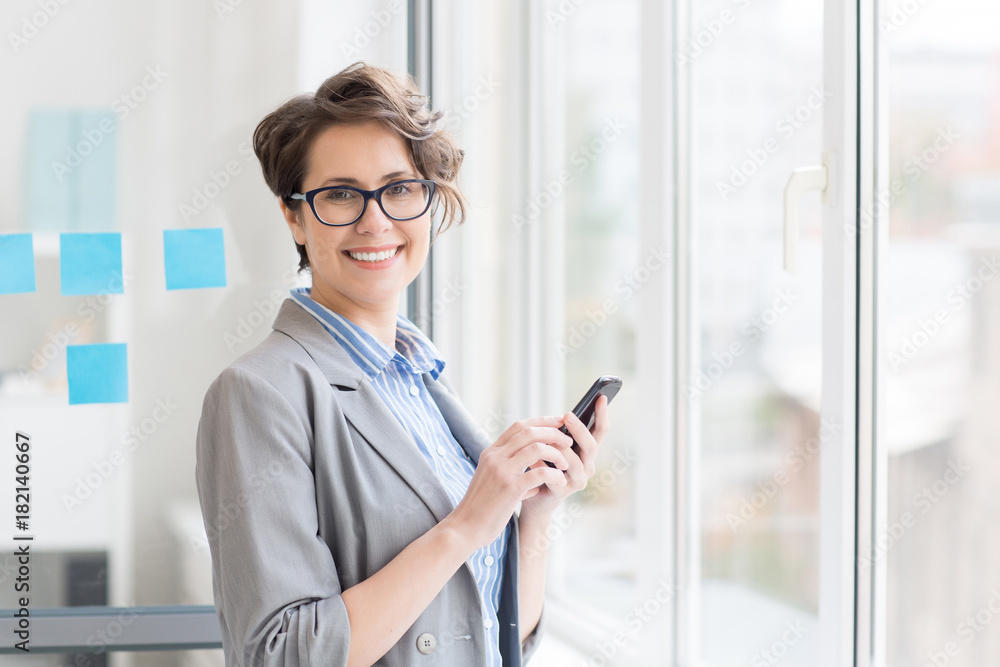 Happy businesswoman with smartphone looking at camera in office Happy businesswoman with smartphone looking at camera in office