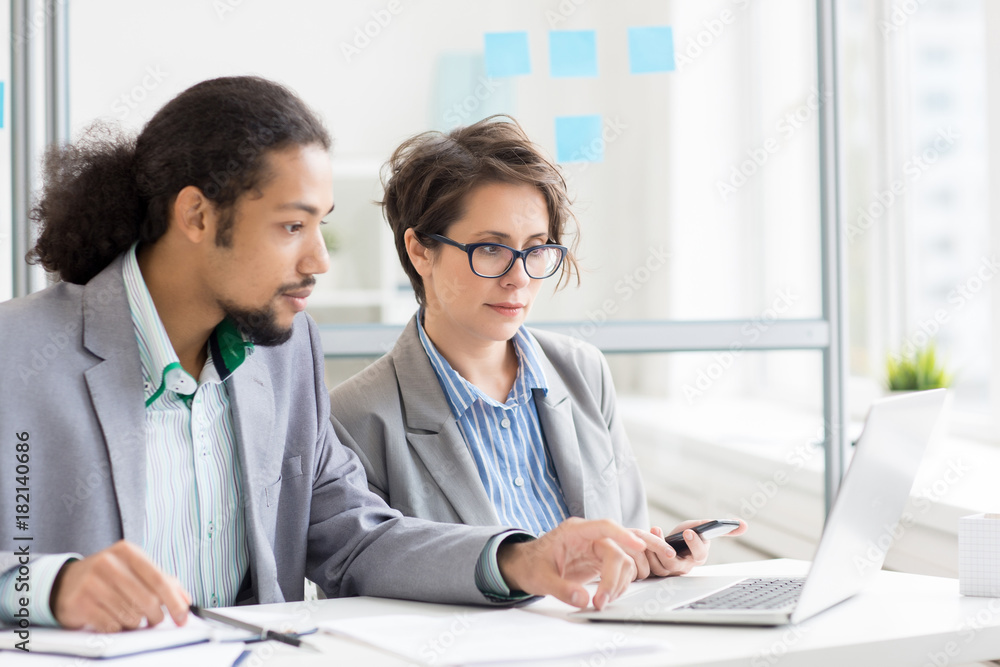 Young man and woman analyzing online information by workplace Young man and woman analyzing online information by workplace