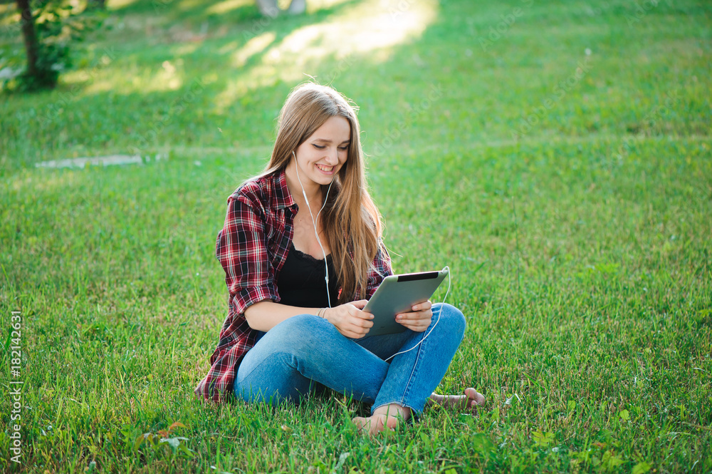 Young woman using tablet outdoor sitting on grass, smiling. Young woman using tablet outdoor sitting on grass, smiling.