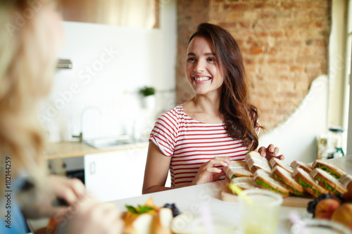 Happy girl looking at her friend in the kitchen while preparing food for home party