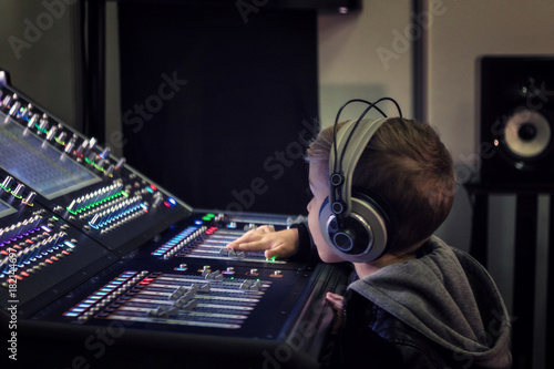 Small boy with headphones editing music on sound mixer in a studio.