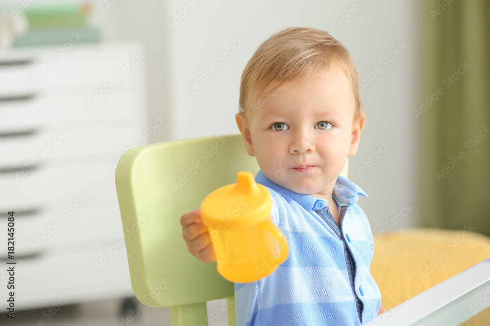 Adorable baby sitting at table with drinking bottle indoors Adorable baby sitting at table with drinking bottle indoors