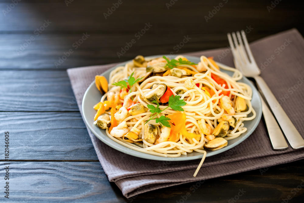 Seafood noodles. Pasta with seafood and vegetables - shrimps, mussels, tomato and spinach on a dark background. Selective focus