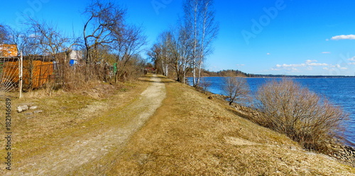 Panoramic view of grassy riverside with unpaved road 