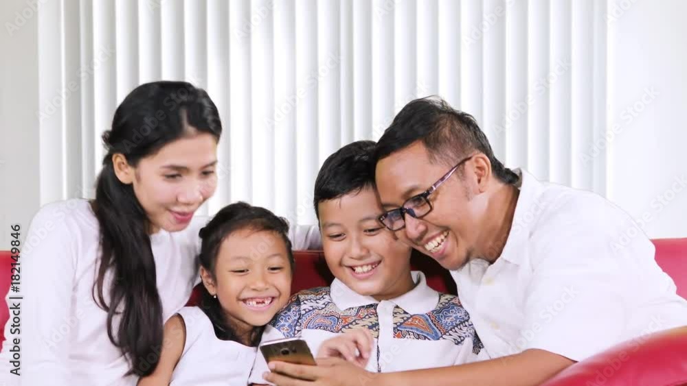 Happy family using a smartphone together while chatting and sitting on the sofa in the living room at home Happy family using a smartphone together while chatting and sitting on the sofa in the living room at home