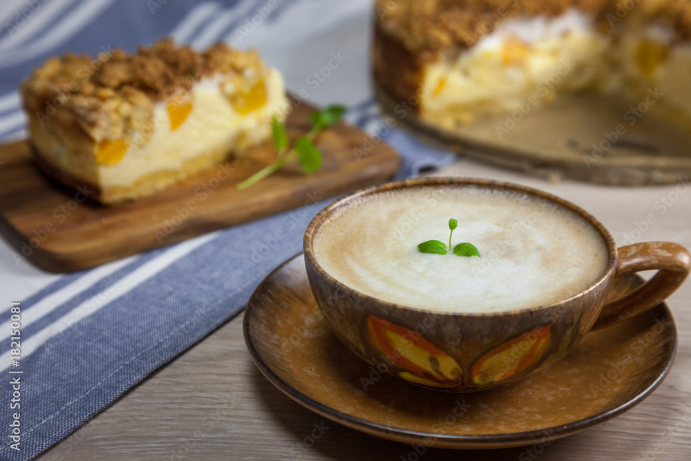 Cup of coffee with the slice of cheesecake with peach on the wooden cutting board and cake on the background Cup of coffee with the slice of cheesecake with peach on the wooden cutting board and cake on the background