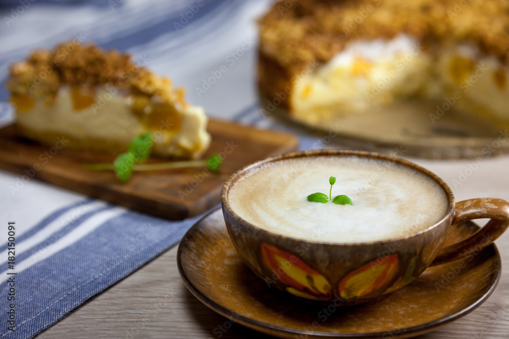 Cup of coffee with the slice of cheesecake with peach on the wooden cutting board and cake on the background Cup of coffee with the slice of cheesecake with peach on the wooden cutting board and cake on the background