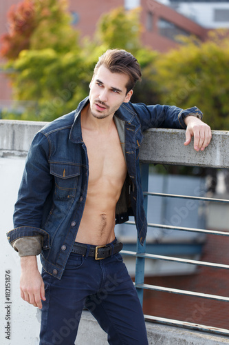 Sexy young caucasian man posing at railing outdoors