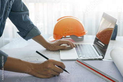 architect working with sketch on blueprint of construction in office, computer laptop and construction tools on wooden table