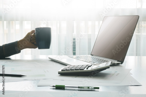 accountant tools with calculator and laptop on wooden table,female hands holding cups of coffee as background, finances and business concept.