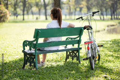 Woman relaxing on park bench under a tree next to a bicycle