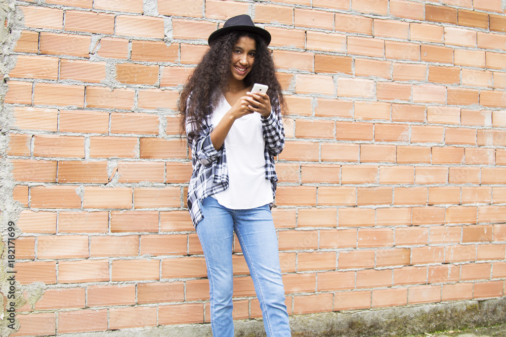 afro woman with hat with mobile phone on the brick wall afro woman with hat with mobile phone on the brick wall