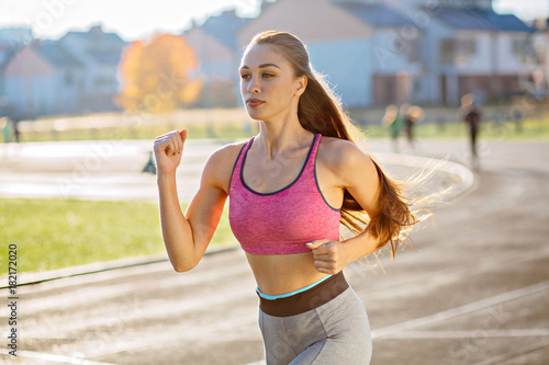 Fototapeta Naklejka Na Ścianę i Meble -  Young fitness woman running during sunny morning on stadium track