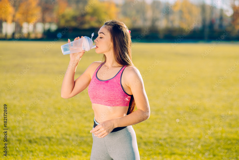Fitness sporty female in sportswear at stadium outdoor sports. Tired thirsty woman drinking water from sport bottle. Fitness sporty female in sportswear at stadium outdoor sports. Tired thirsty woman drinking water from sport bottle.