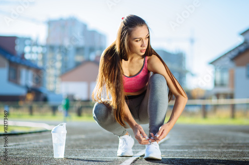 Woman tying lace on her sneakers on a running stadium track. Close up