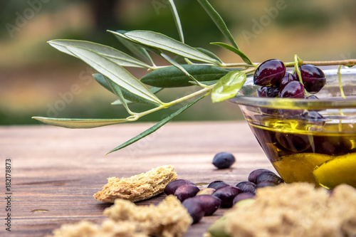 Bowl with extra virgin olive oil, olives, a fresh branch of olive tree and cretan rusk dakos close up, Crete, Greece. photo