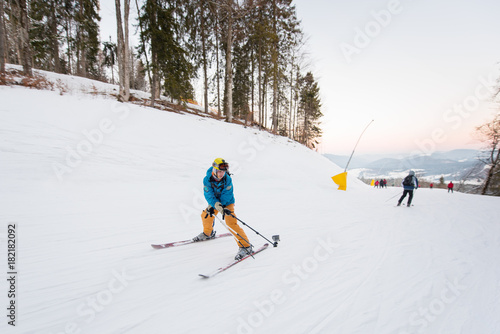 Guy on skis riding down the mountain slope and taking selfie with stick on the winter resort