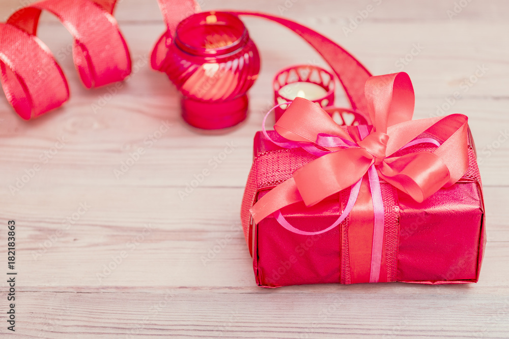 Festive gift box with a bow of red color. Lies on a white background. Next to pink flowers. Festive gift box with a bow of red color. Lies on a white background. Next to pink flowers.