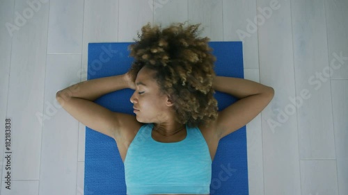 From above shot of young ethnic model in sportive top lying on back with hands under head and looking away in contemplation relaxing after workout. photo