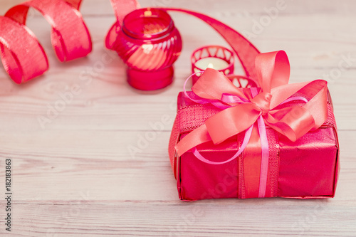 Festive gift box with a bow of red color. Lies on a white background. Next to pink flowers.