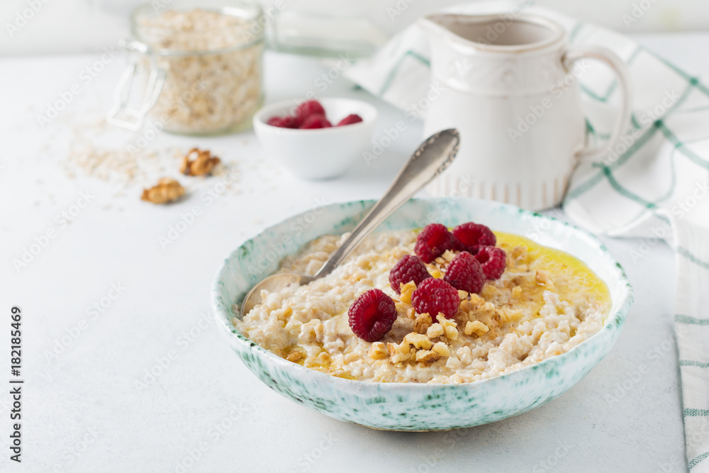 Oatmeal porridge with fresh raspberries, walnuts and butter in a ceramic plate on a light stone or concrete background. Selective focus. Oatmeal porridge with fresh raspberries, walnuts and butter in a ceramic plate on a light stone or concrete background. Selective focus.