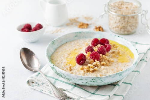 Oatmeal porridge with fresh raspberries, walnuts and butter in a ceramic plate on a light stone or concrete background. Selective focus.