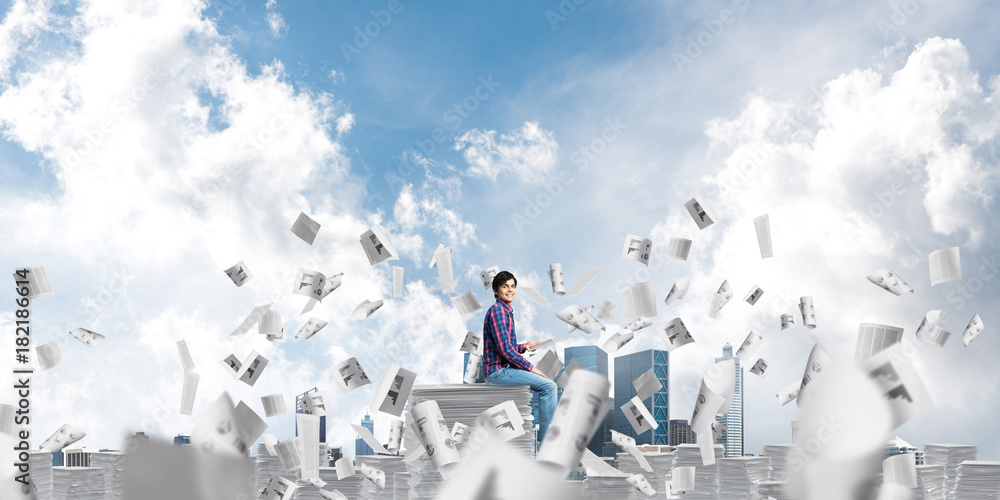 Attractive man sitting on pile of paper documents.