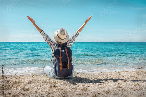 Blonde woman in summer hat with her backpack sitting on the sand