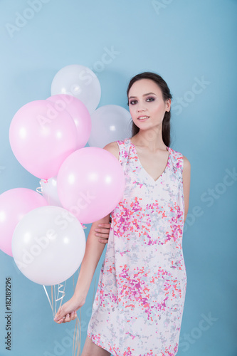 Beautiful young girl in a flower dress holding balloons on a blue background